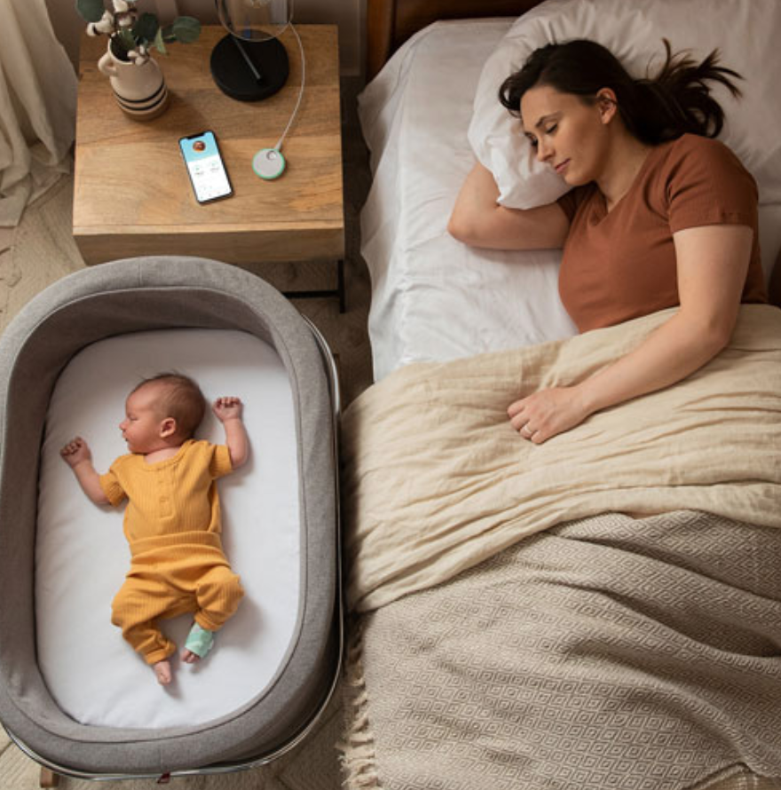 baby sleeping in bassinet with mom beside them in bed.