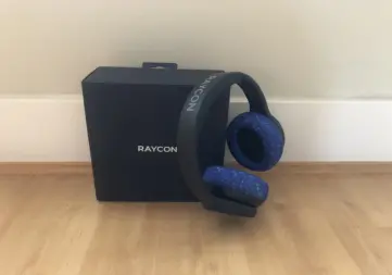 Raycon's The Fitness Headphones with blue ear cushions Raycon The Fitness Headphones with blue ear cushions resting on the Raycon box.