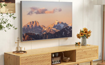 A TV mounted on the wall under a Costeay bamboo TV stand.