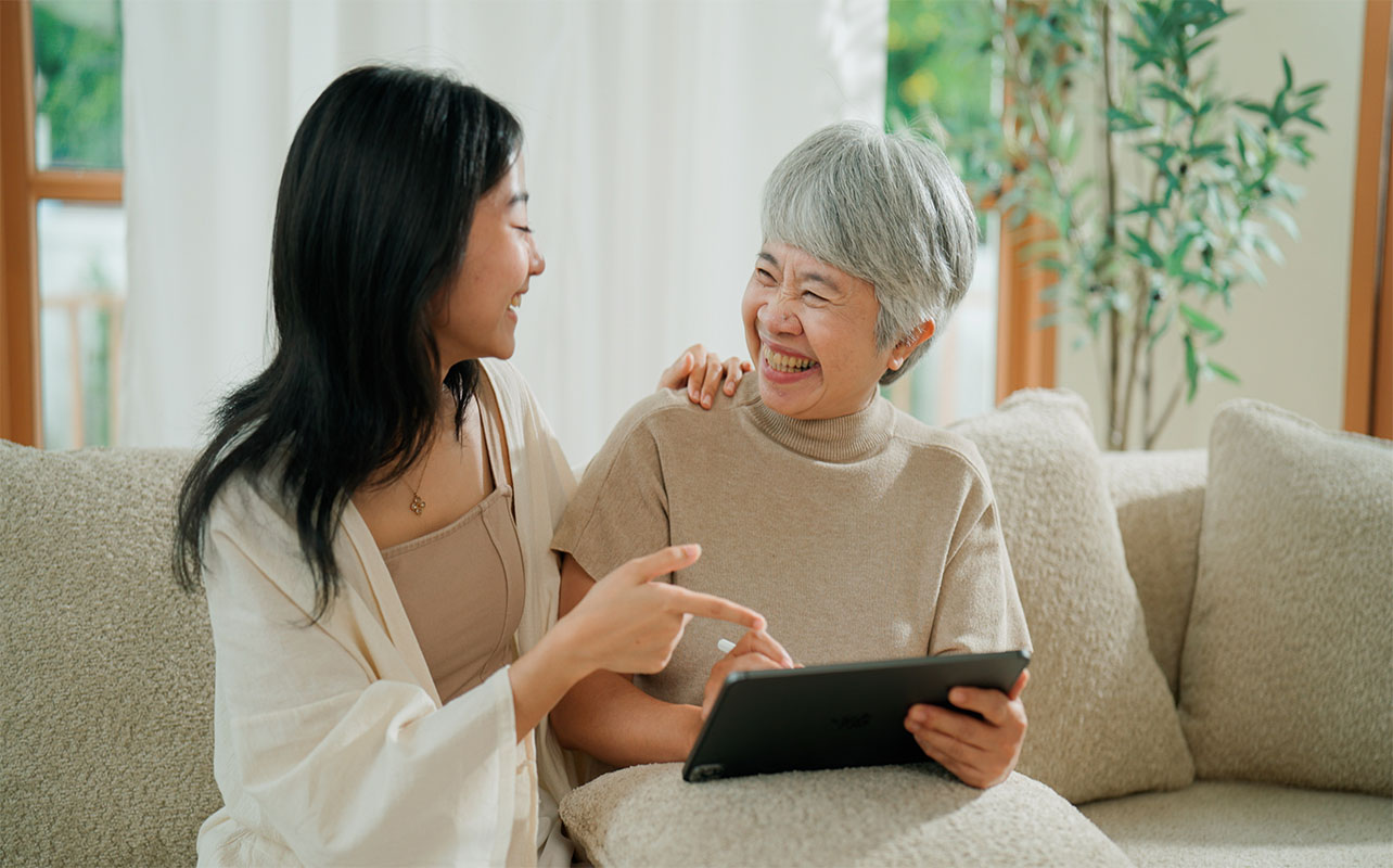 Une jeune femme asiatique apprend à sa mère retraitée à utiliser une tablette numérique dans le salon.