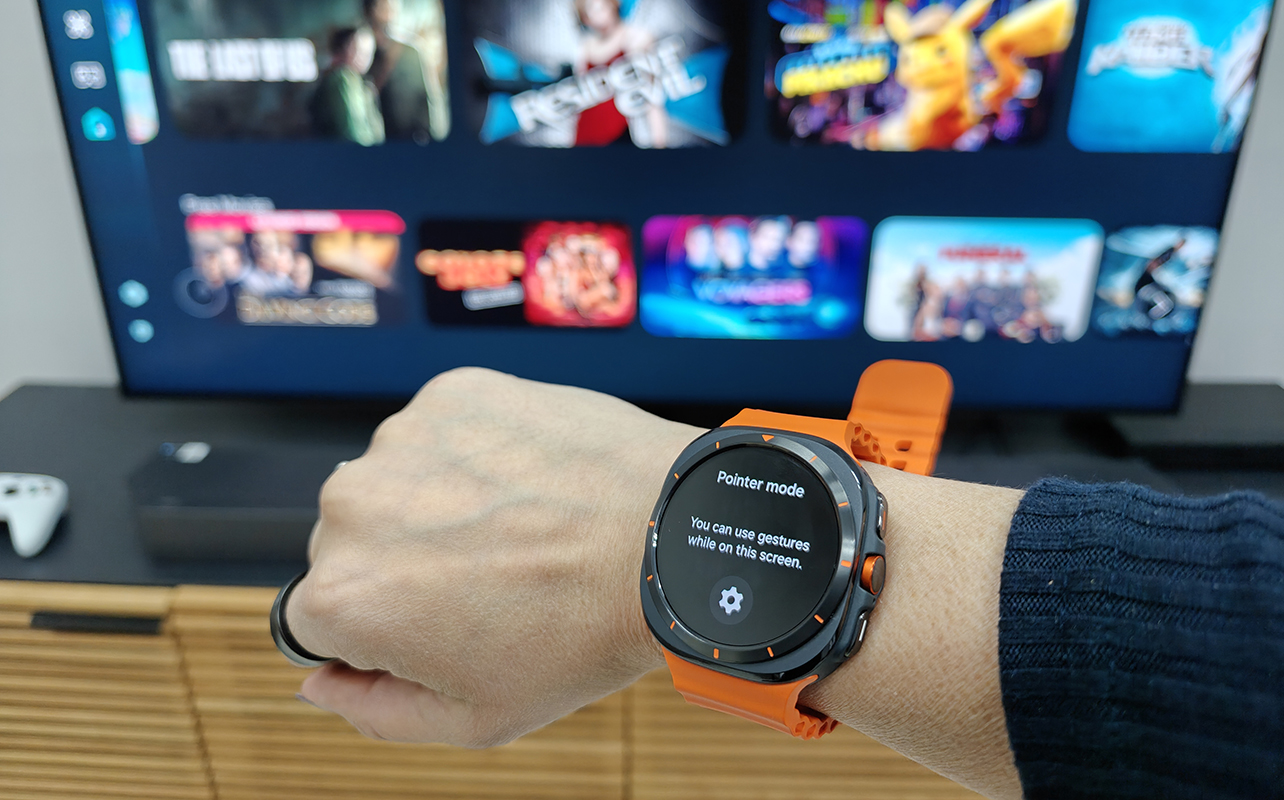 A hand wearing a Samsung Galaxy Watch Ultra in front of a Samsung Neo QLED TV