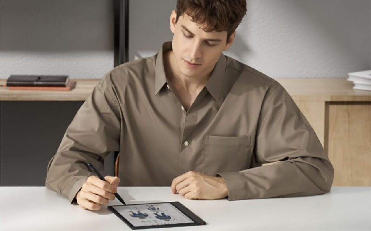 Un homme assis écrivant sur une tablette à encre électronique Note Aie 4 de Boox.