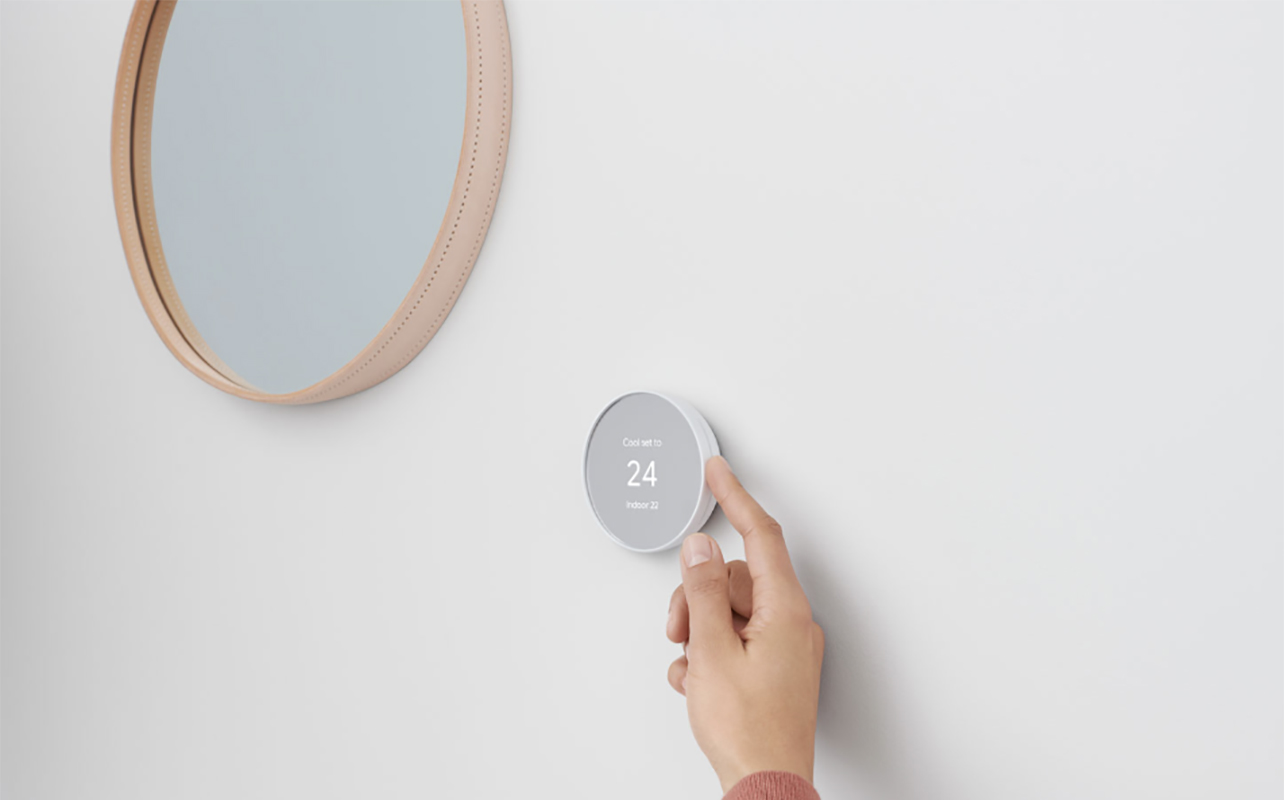 A finger adjusting a Google Nest smart thermostat.