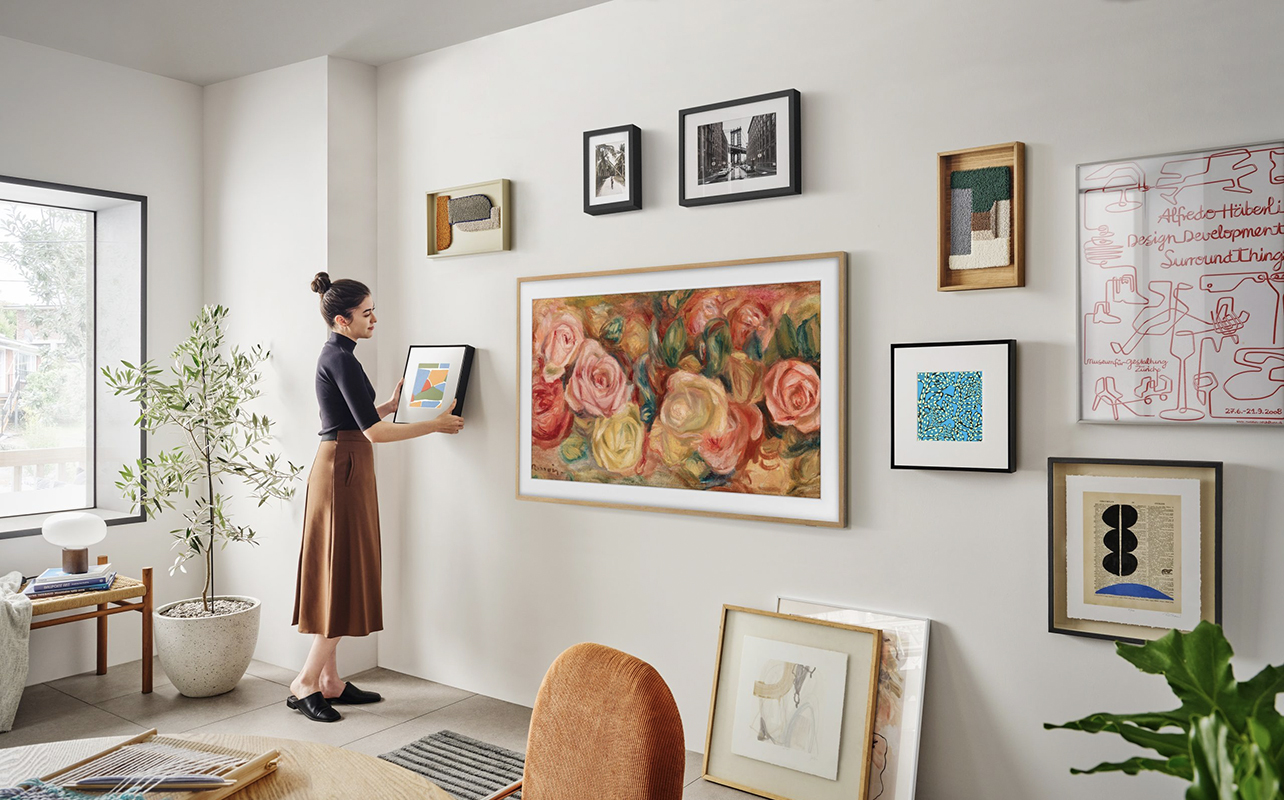 Une femme arrangeant le Music Frame de Samsung autour d'un téléviseur The Frame de Samsung monté au mur.